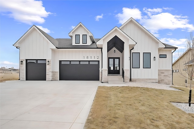 modern farmhouse featuring a garage, concrete driveway, stone siding, french doors, and board and batten siding