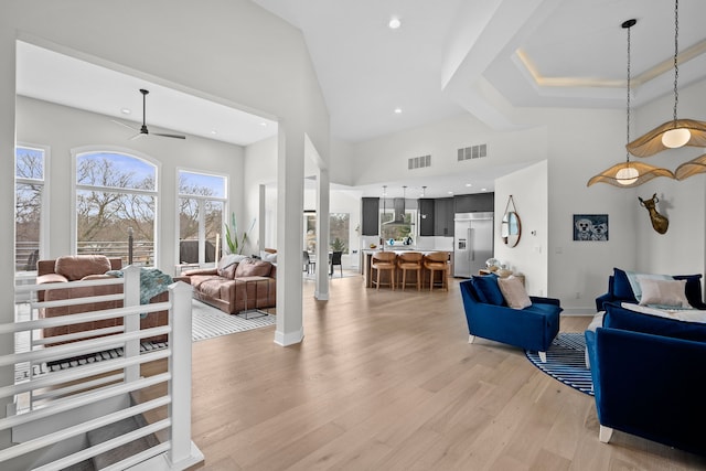 living room featuring light wood finished floors, visible vents, baseboards, and a towering ceiling