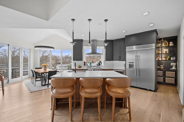 kitchen with light wood-style flooring, island exhaust hood, a kitchen island with sink, stainless steel built in fridge, and light countertops