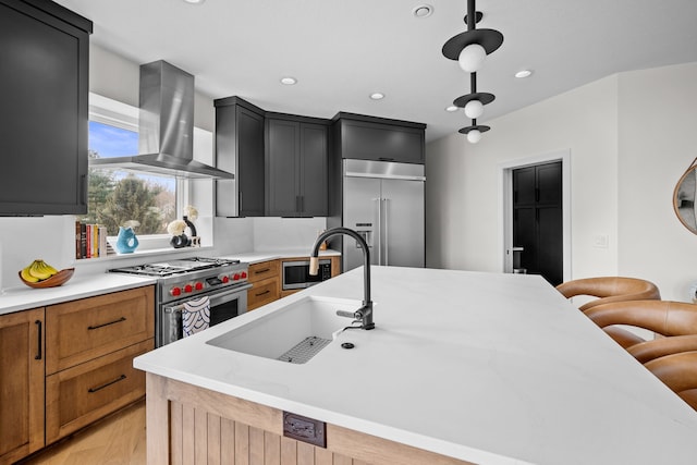 kitchen with a sink, a kitchen breakfast bar, ventilation hood, built in appliances, and dark cabinets