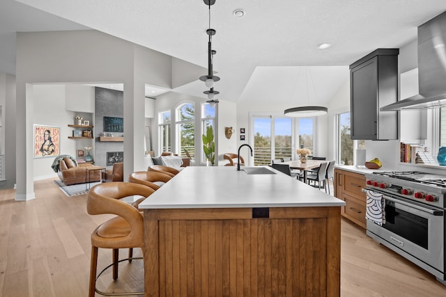 kitchen with a sink, light countertops, wall chimney exhaust hood, light wood-type flooring, and designer range