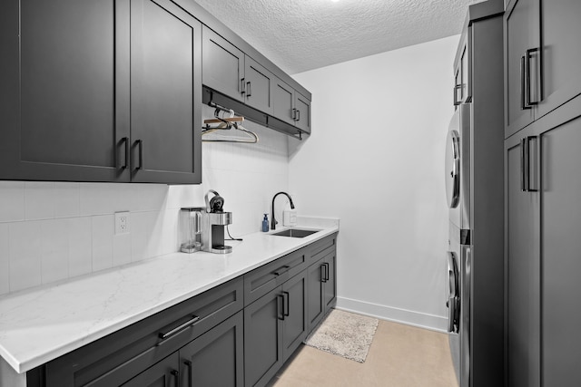 kitchen with tasteful backsplash, baseboards, light stone counters, a textured ceiling, and a sink