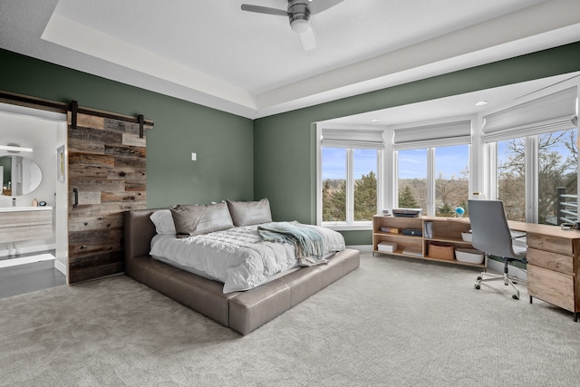 carpeted bedroom with a barn door, ceiling fan, and ensuite bathroom