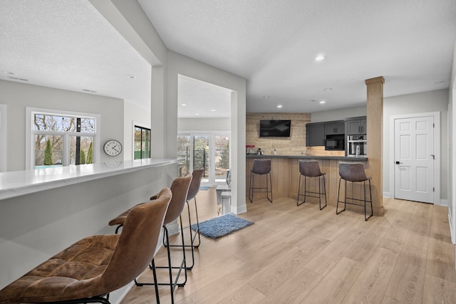 kitchen with a breakfast bar, light wood-style flooring, recessed lighting, black microwave, and stainless steel oven