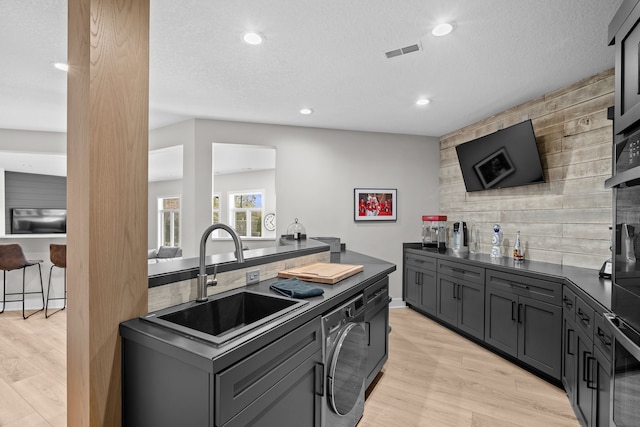 kitchen with dark countertops, visible vents, light wood-type flooring, washer / clothes dryer, and a sink