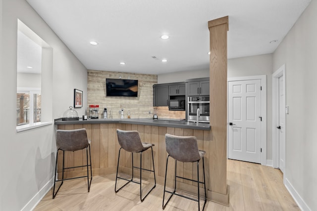 kitchen featuring a breakfast bar area, light wood finished floors, gray cabinetry, black microwave, and backsplash