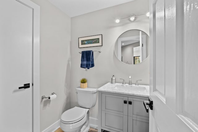 half bath with baseboards, toilet, and vanity