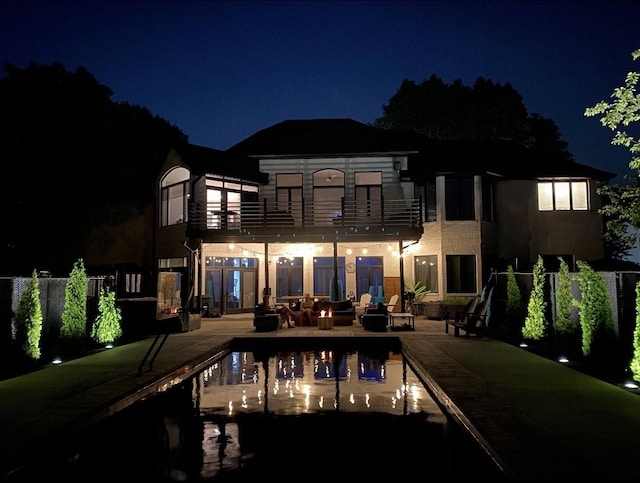 back of house at night with a patio area, a fenced in pool, and a balcony