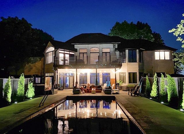 back of house at night with a patio area, a balcony, a fire pit, and stucco siding