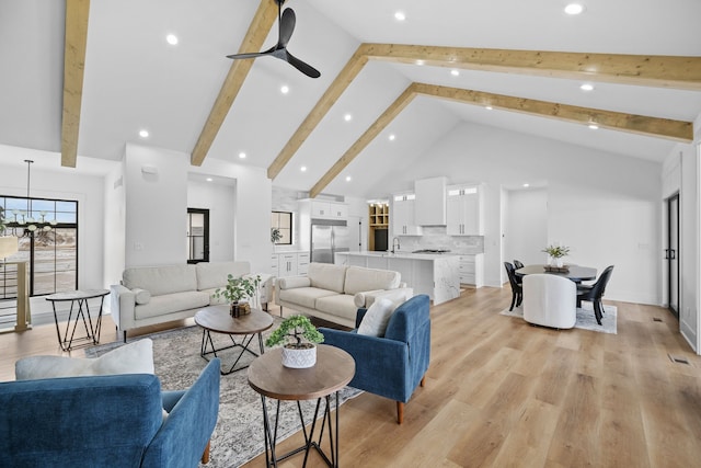 living room with beam ceiling, high vaulted ceiling, light wood-style flooring, ceiling fan with notable chandelier, and baseboards