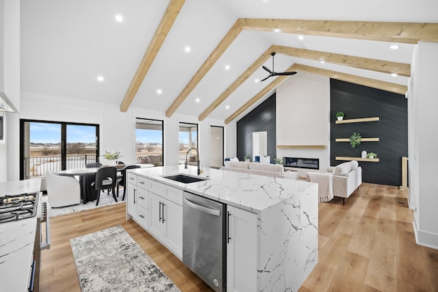 kitchen with a sink, light stone counters, stainless steel dishwasher, a glass covered fireplace, and white cabinets