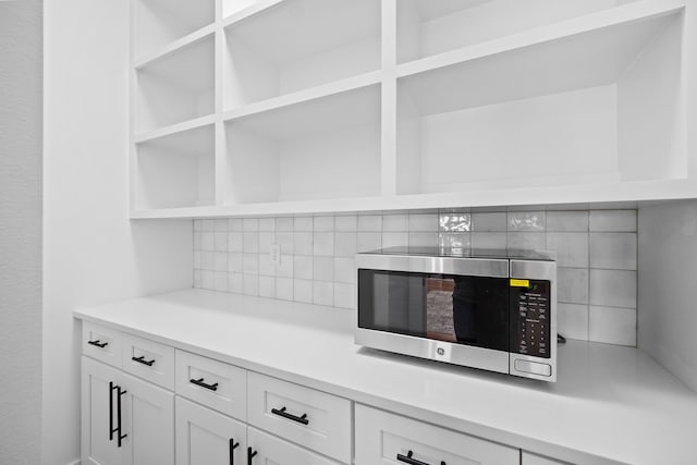 interior details featuring open shelves, stainless steel microwave, white cabinets, light countertops, and decorative backsplash