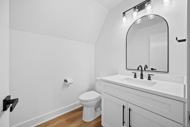 half bathroom with baseboards, toilet, vaulted ceiling, wood finished floors, and vanity