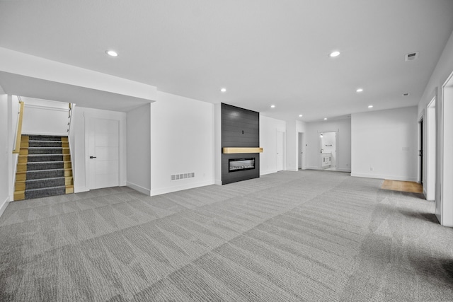 unfurnished living room with visible vents, recessed lighting, a fireplace, stairs, and light carpet