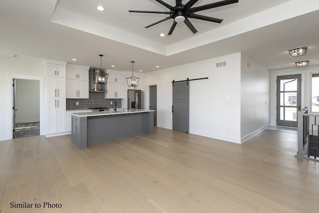 kitchen featuring white cabinets, stainless steel fridge, hanging light fixtures, a barn door, and a spacious island