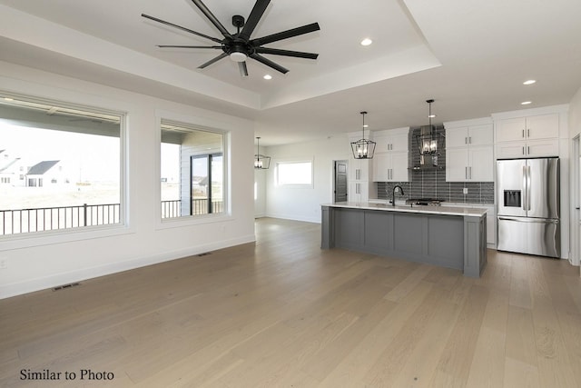 kitchen featuring decorative light fixtures, a large island with sink, stainless steel fridge with ice dispenser, and white cabinets