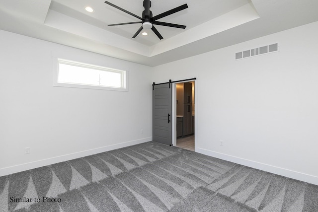 unfurnished room with carpet, a raised ceiling, and a barn door