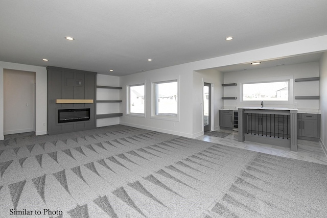 unfurnished living room with sink, a wealth of natural light, wine cooler, and a fireplace