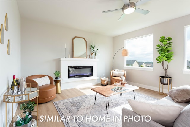 living area with wood finished floors, ceiling fan, a glass covered fireplace, and baseboards