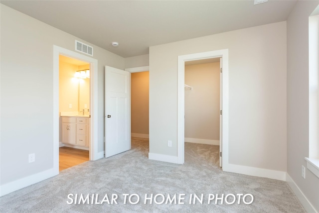 unfurnished bedroom with light colored carpet, connected bathroom, and a spacious closet