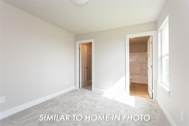 unfurnished bedroom with carpet, baseboards, a walk in closet, and ensuite bath