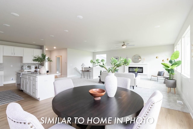 dining space featuring light wood finished floors, ceiling fan, baseboards, and a glass covered fireplace