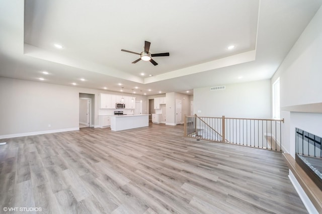 15015 Springbrook Trl, Urbandale, IA 50323 - unfurnished living room featuring a tray ceiling, ceiling fan, recessed lighting, and light wood-style floors