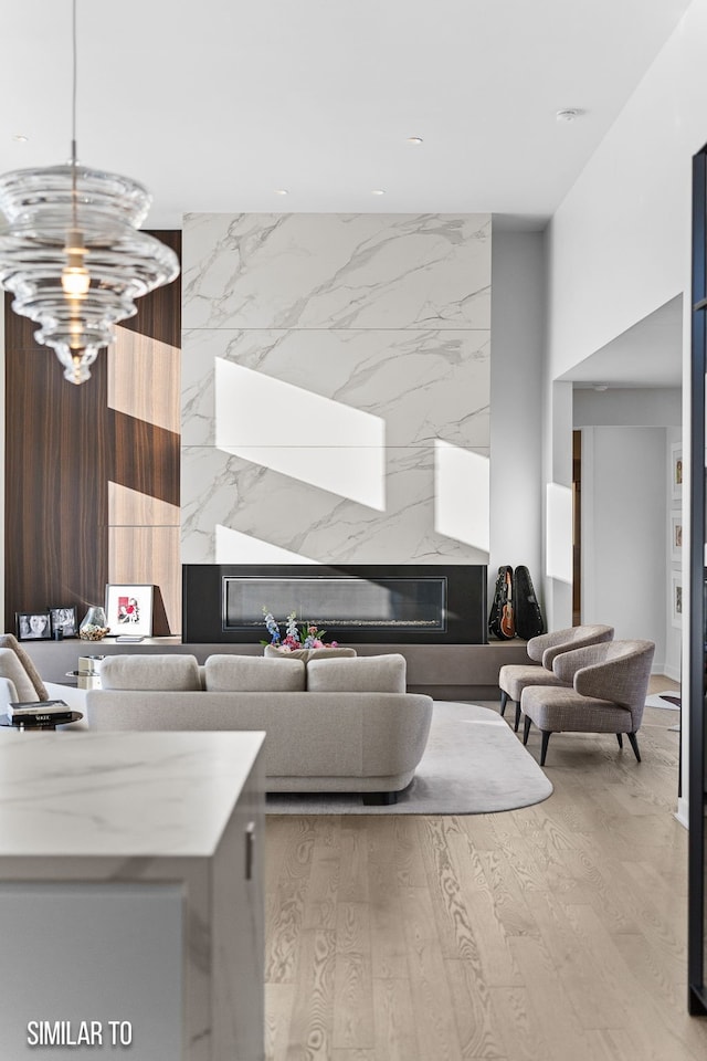 living room with an inviting chandelier, a high end fireplace, and light wood finished floors