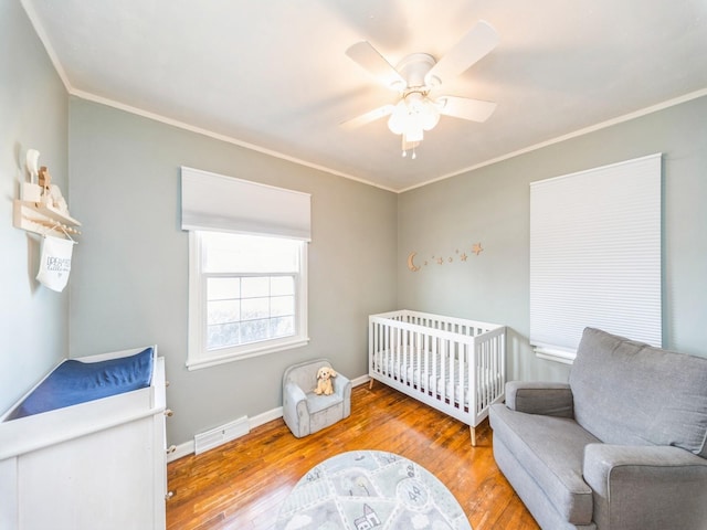 bedroom featuring ornamental molding, a nursery area, ceiling fan, and light wood-type flooring