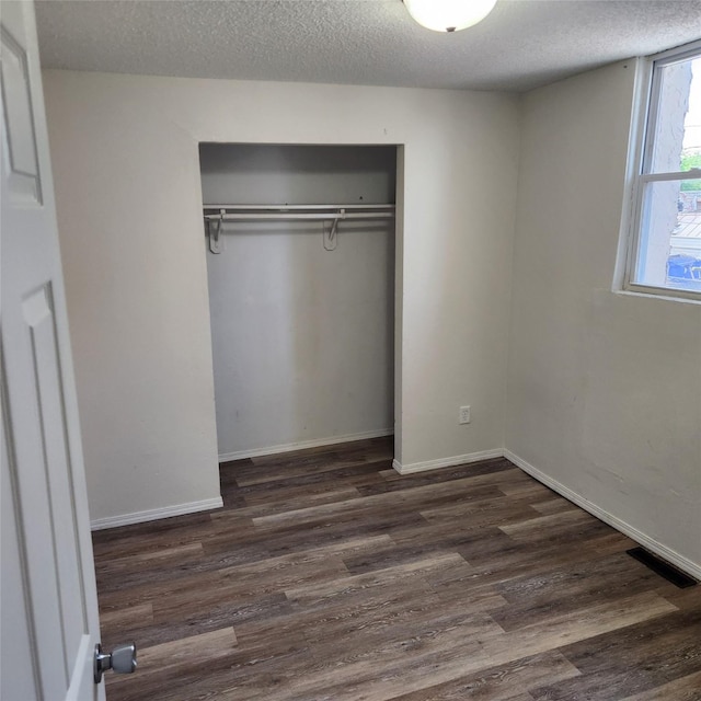 unfurnished bedroom with dark hardwood / wood-style floors, a textured ceiling, and a closet