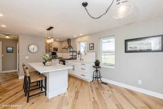 kitchen featuring a center island, gas stove, white cabinetry, wall chimney range hood, and light wood-type flooring