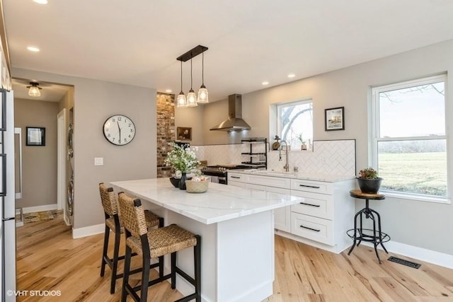 kitchen with light stone counters, a kitchen island, backsplash, wall chimney exhaust hood, and a kitchen bar