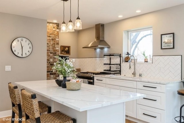 kitchen with light stone countertops, a sink, a kitchen breakfast bar, a center island, and wall chimney exhaust hood