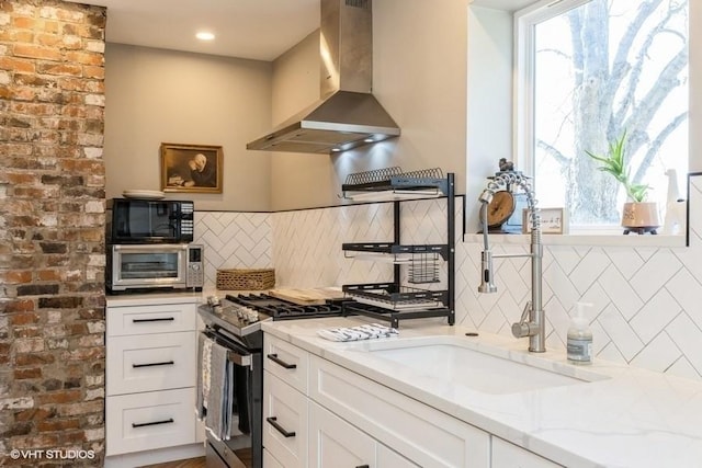 kitchen with white cabinets, stainless steel range with gas stovetop, light stone countertops, black microwave, and wall chimney exhaust hood