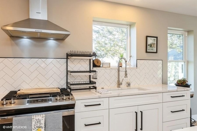 kitchen featuring a sink, white cabinets, wall chimney range hood, decorative backsplash, and stainless steel gas stove