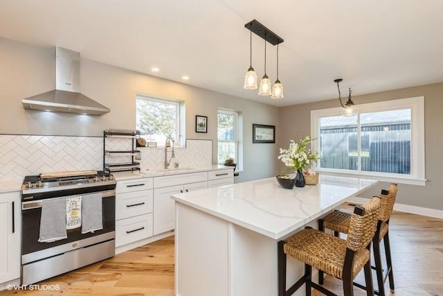 kitchen featuring wall chimney exhaust hood, a kitchen island, stainless steel range with gas stovetop, white cabinetry, and a sink