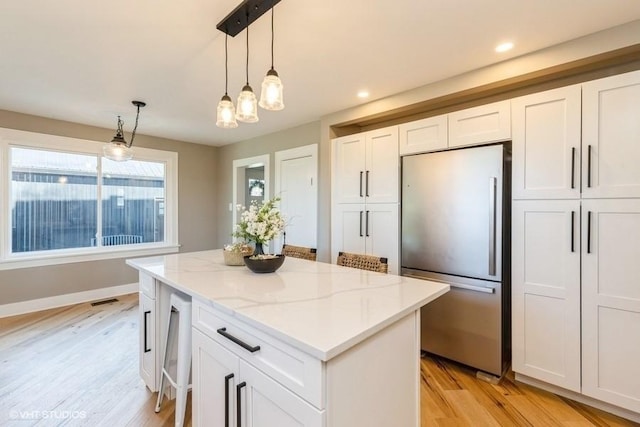 kitchen featuring light stone counters, light wood-style floors, freestanding refrigerator, white cabinets, and a kitchen island