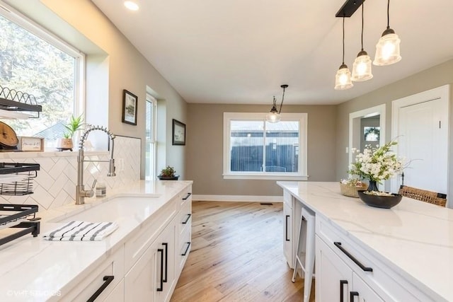 kitchen featuring light stone counters, a sink, white cabinets, backsplash, and light wood finished floors