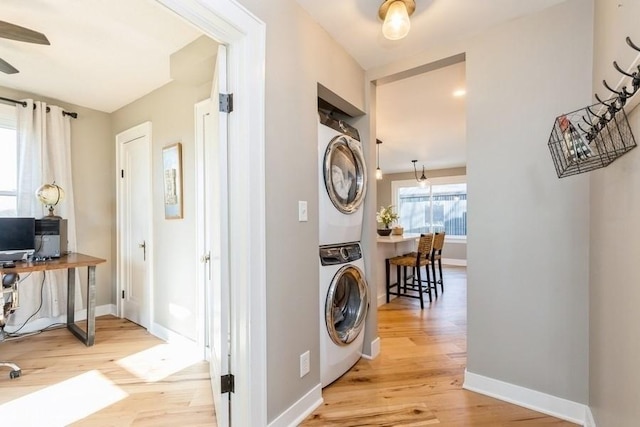 laundry area featuring laundry area, baseboards, ceiling fan, stacked washer / drying machine, and light wood-type flooring