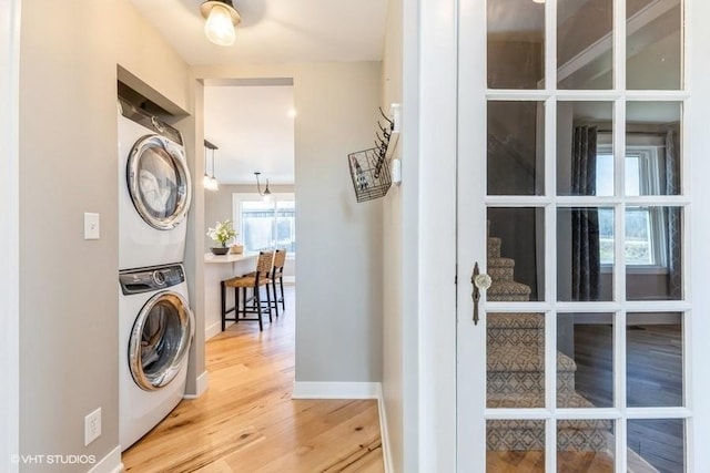 laundry area with laundry area, stacked washer / dryer, wood finished floors, and baseboards