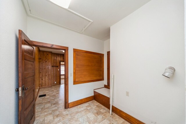 corridor with visible vents, attic access, baseboards, and stone finish floor