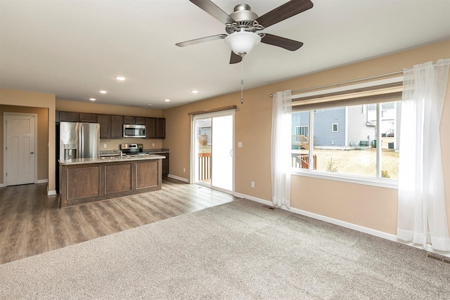 kitchen with sink, dark brown cabinets, light carpet, a center island with sink, and stainless steel appliances