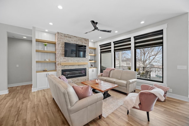 living room with built in shelves, a brick fireplace, ceiling fan, and light hardwood / wood-style flooring