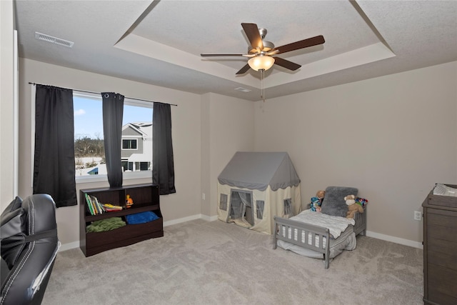 bedroom with light carpet, a textured ceiling, ceiling fan, and a tray ceiling