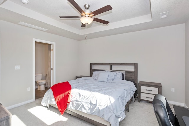 carpeted bedroom with visible vents, baseboards, a tray ceiling, and connected bathroom