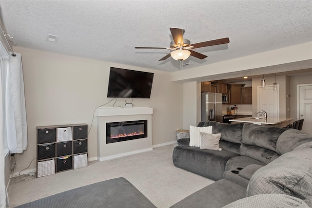 living area with ceiling fan, a glass covered fireplace, a textured ceiling, and light colored carpet