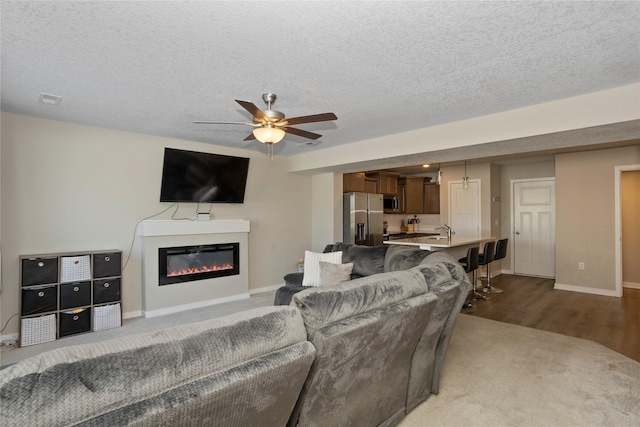 living room featuring ceiling fan, hardwood / wood-style floors, sink, and a textured ceiling