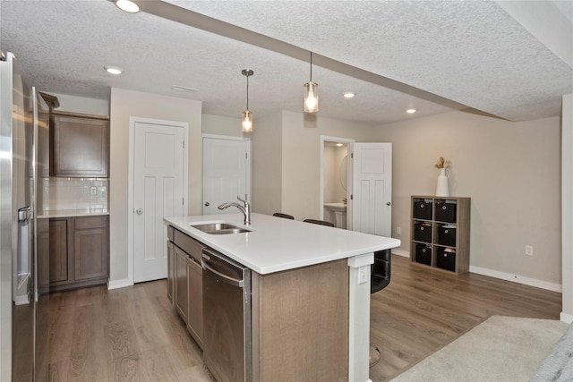 kitchen with dark brown cabinetry, sink, appliances with stainless steel finishes, pendant lighting, and a kitchen island with sink