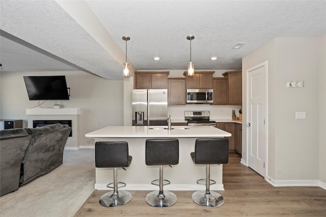 kitchen featuring a sink, open floor plan, a breakfast bar, stainless steel appliances, and light countertops