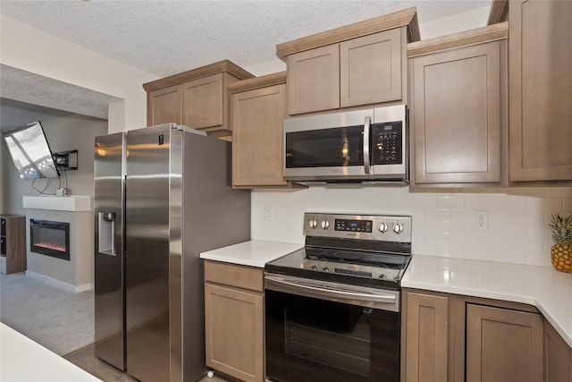 kitchen featuring a textured ceiling, a glass covered fireplace, stainless steel appliances, light countertops, and backsplash